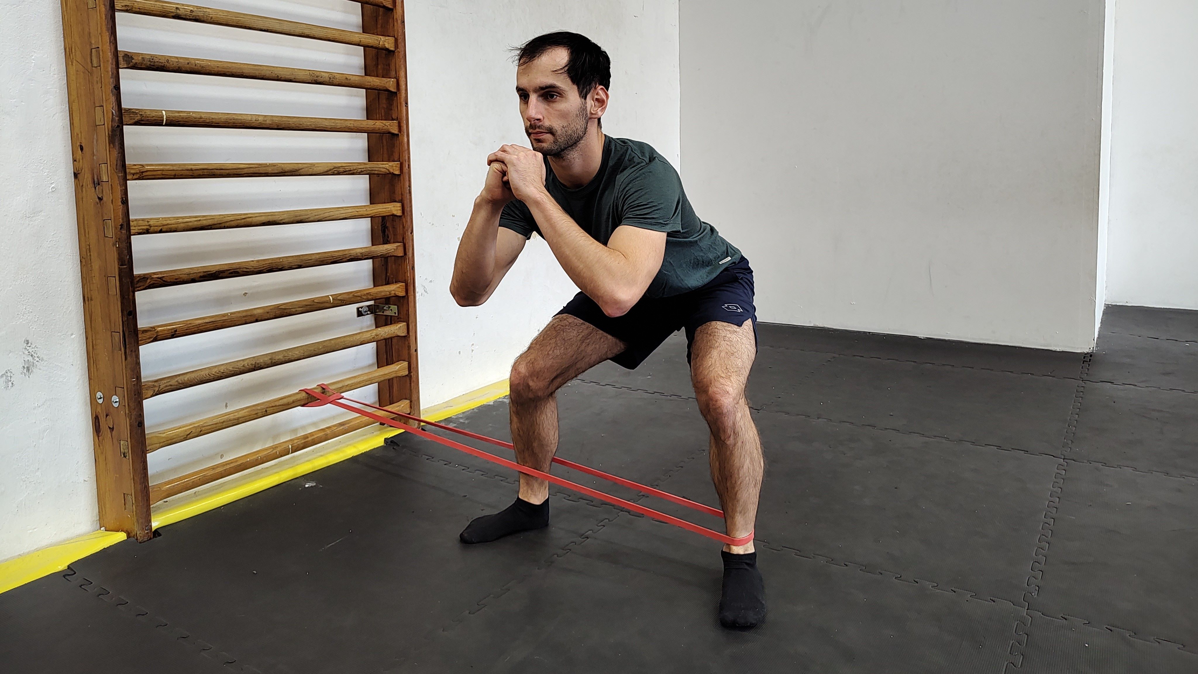 Muž v tělocvičně cvičí dřep s úkrokem do strany s expandérem.